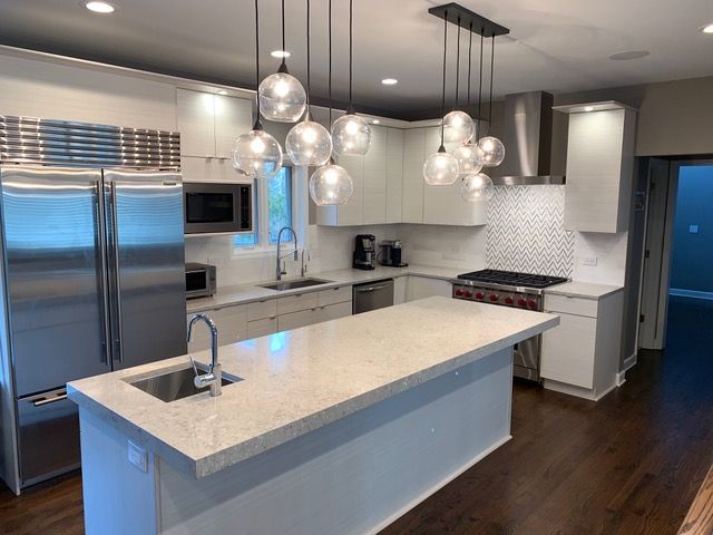 Modern kitchen with a large quartz-topped island, stainless steel appliances, white cabinets, and glass pendant lights.