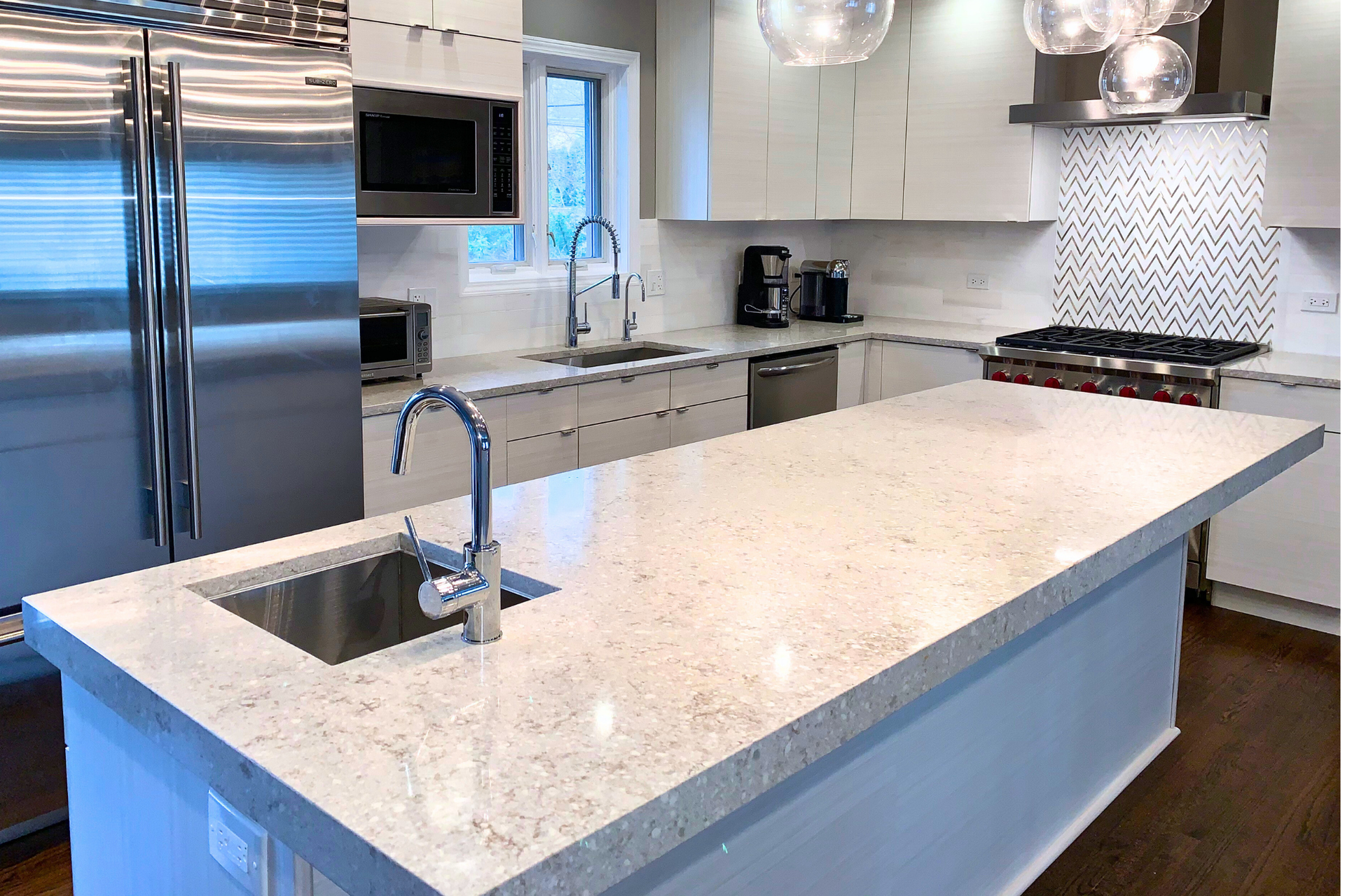 Modern kitchen with white cabinets, a large quartz-topped island, stainless steel appliances, and wood flooring.