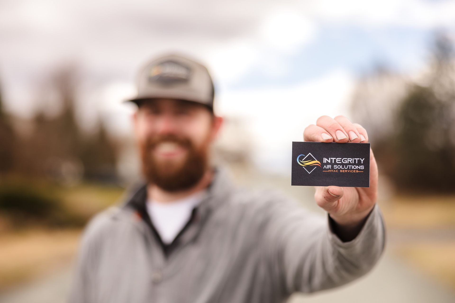 Smiling man outdoors holding up a business card toward the camera.