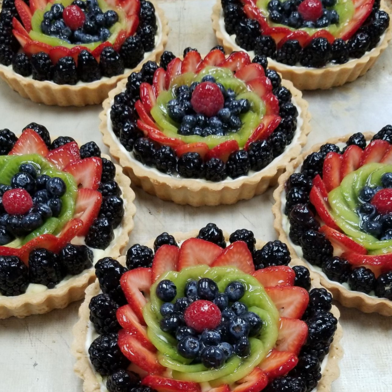 Six fruit tarts topped with blackberries, kiwi, strawberries, blueberries, and a single raspberry in the center.