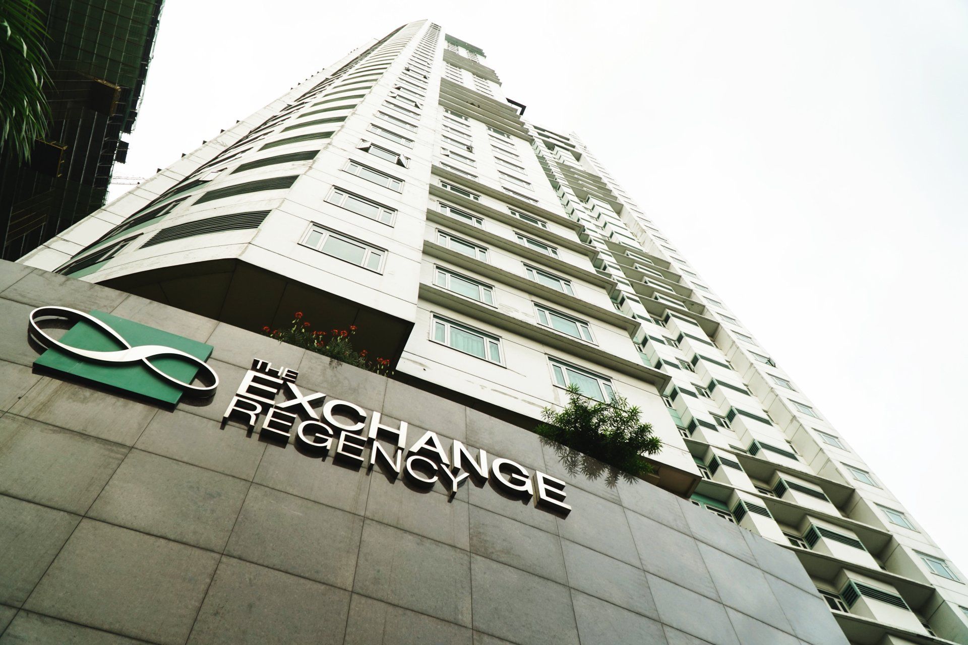 The Exchange Regency skyscraper with a teal logo against a cloudy sky.