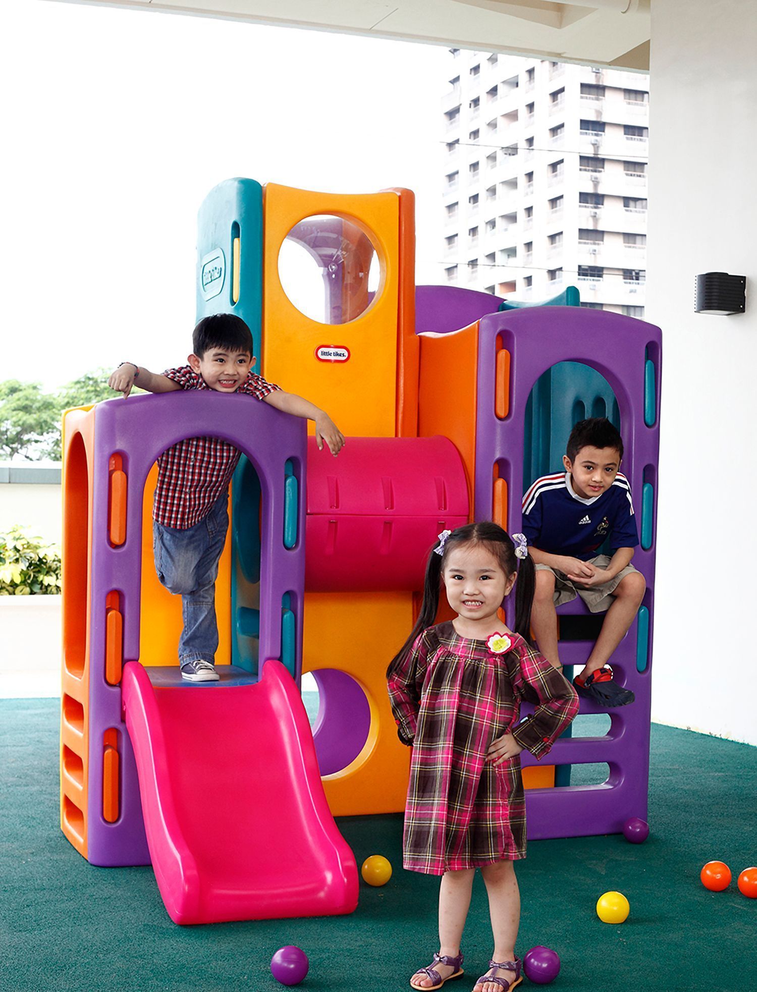 Children on a colorful playground structure, with a girl standing in front and two kids playing on the slides.