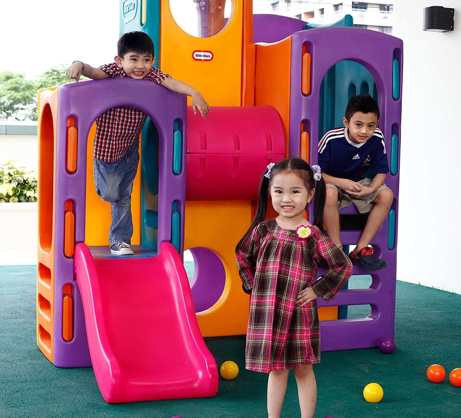 A girl in a plaid dress and two boys are standing in front of a playground of a hotel in Pasig