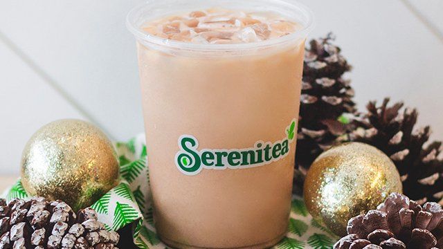 A cup of Serenitea is sitting on a table next to pine cones.