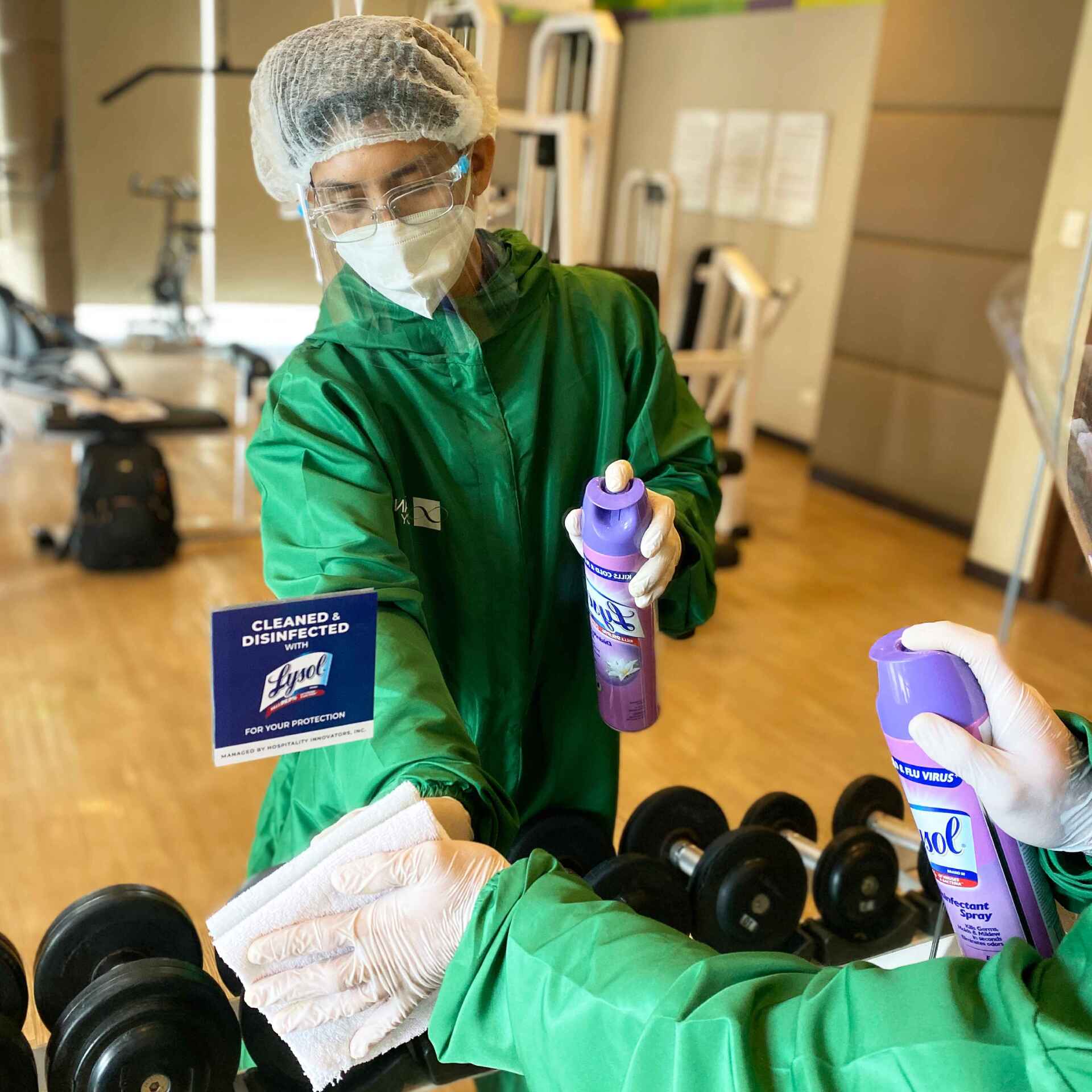 A person wearing a mask is cleaning a dumbbell in a gym.