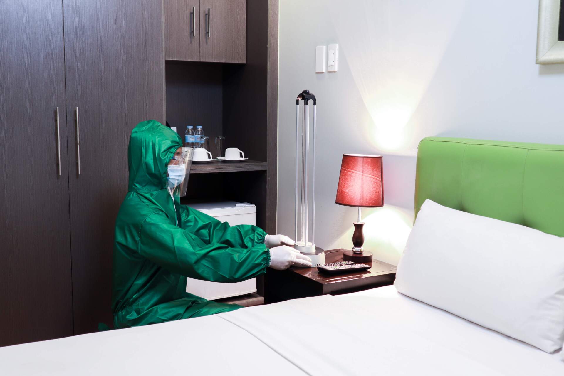 A person in a protective suit is cleaning a hotel room.