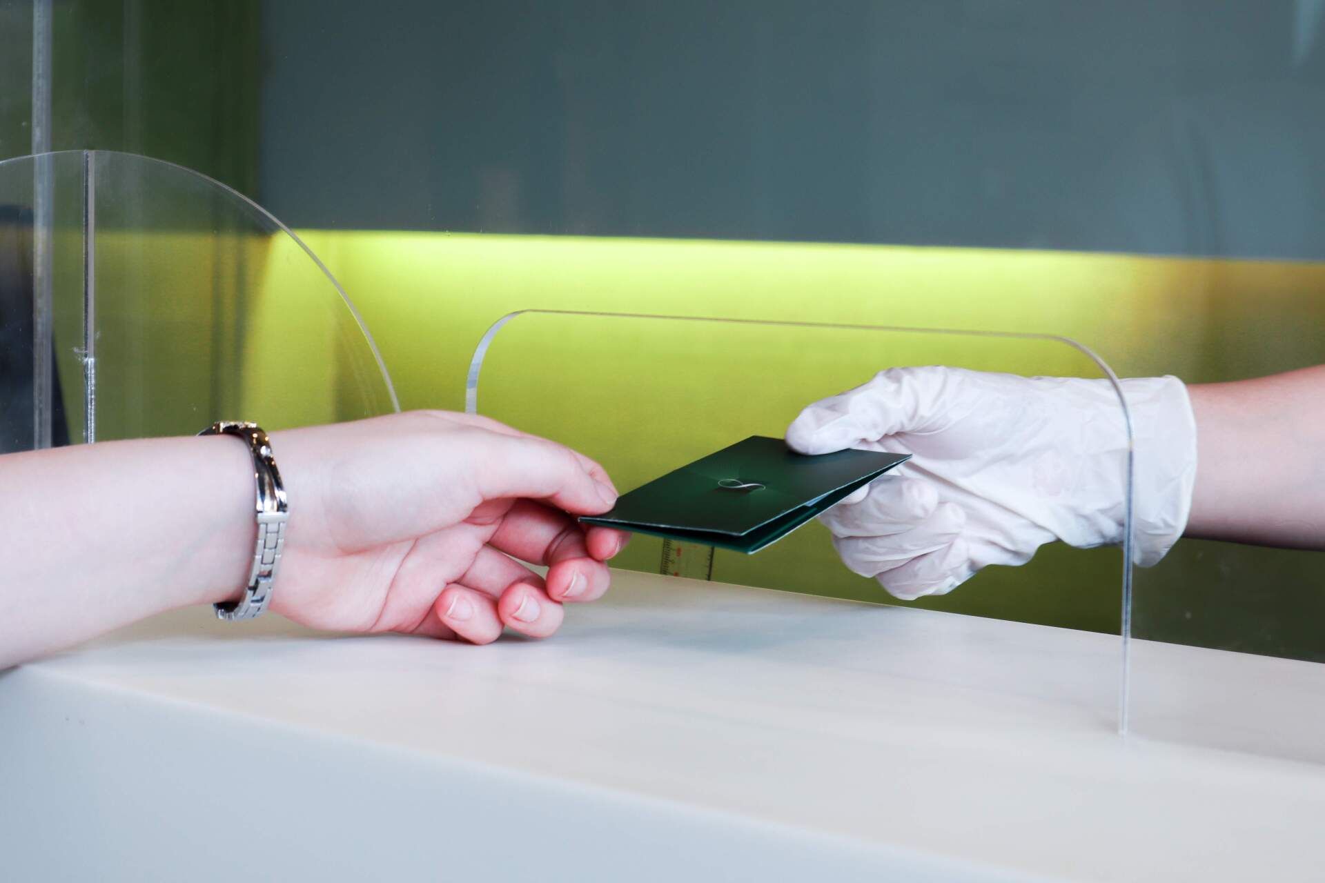 A person wearing white gloves is handing a passport to another person.
