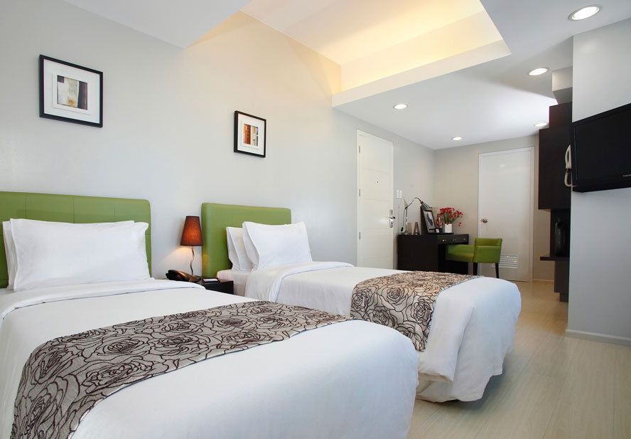 Two twin beds in a modern room, green headboards, white bedding, desk in the background.