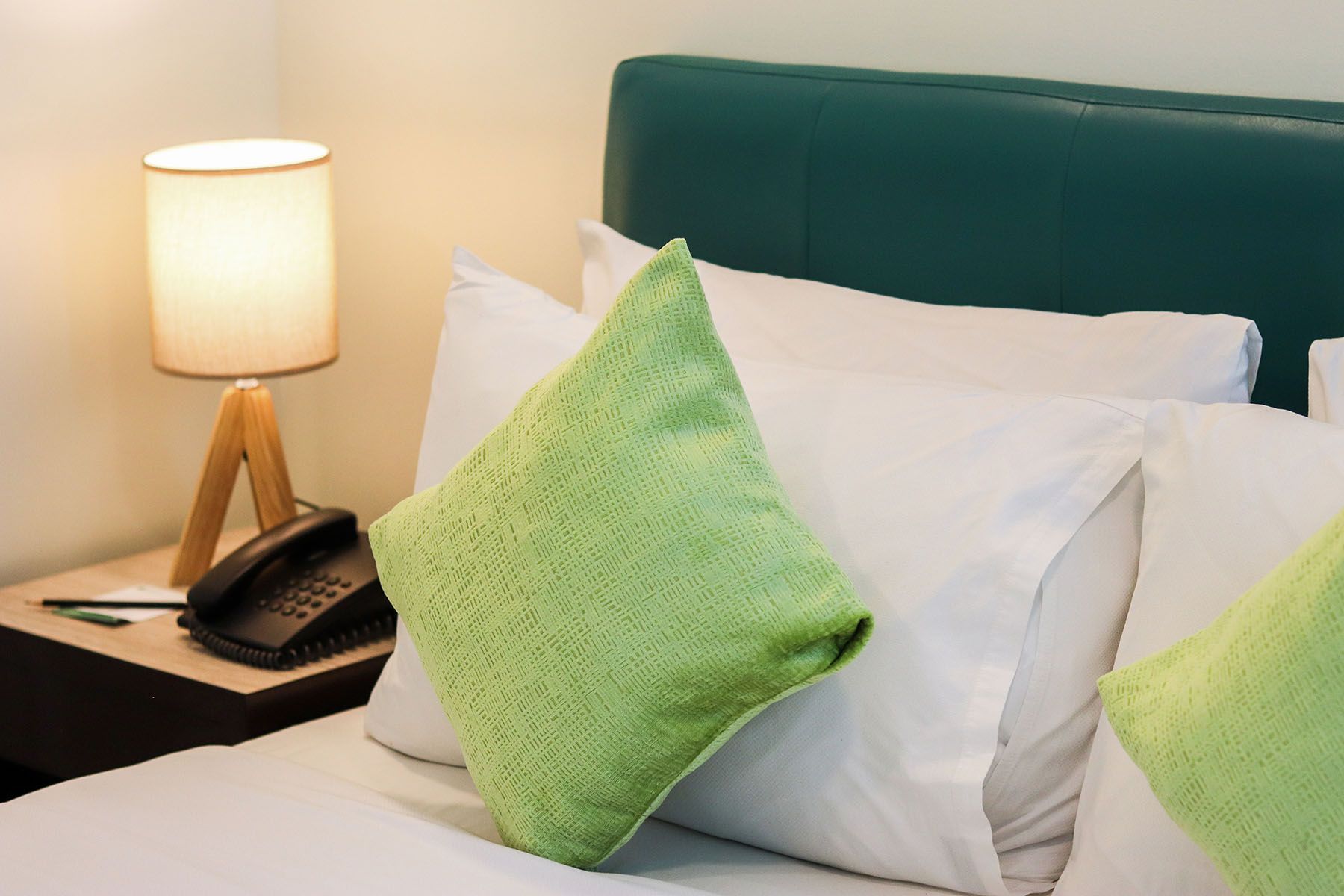 A bed with white sheets and green pillows in a hotel room