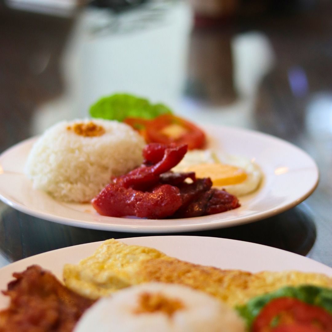 Plated breakfast rice with eggs, sausage, and garnish on a table, with a second plate in the foreground