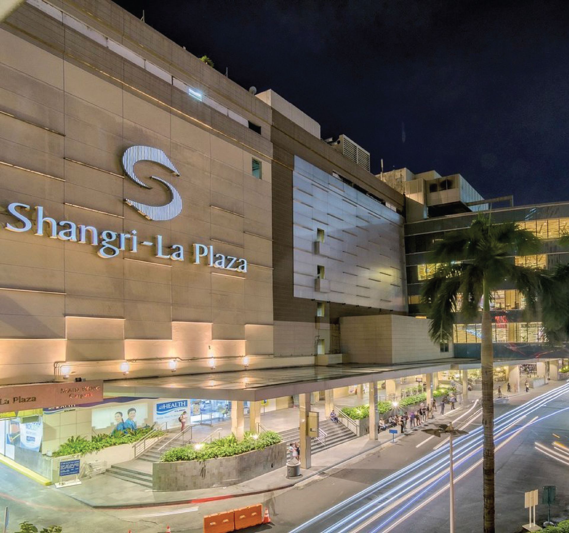 Shangri-La Plaza building facade at night with illuminated signage and palm tree.