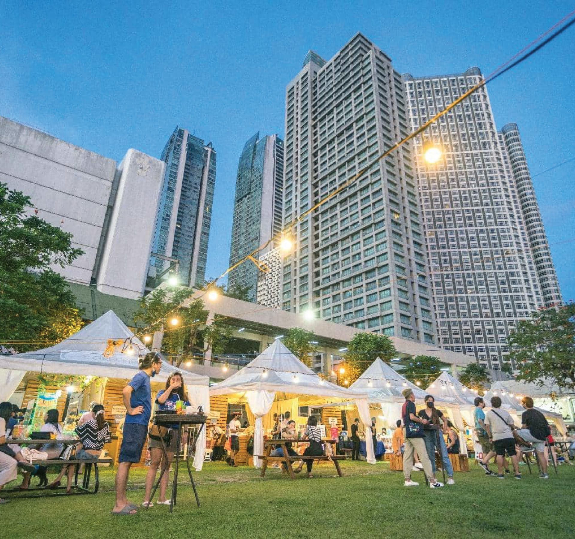A group of people are gathered in a park in front of tall buildings