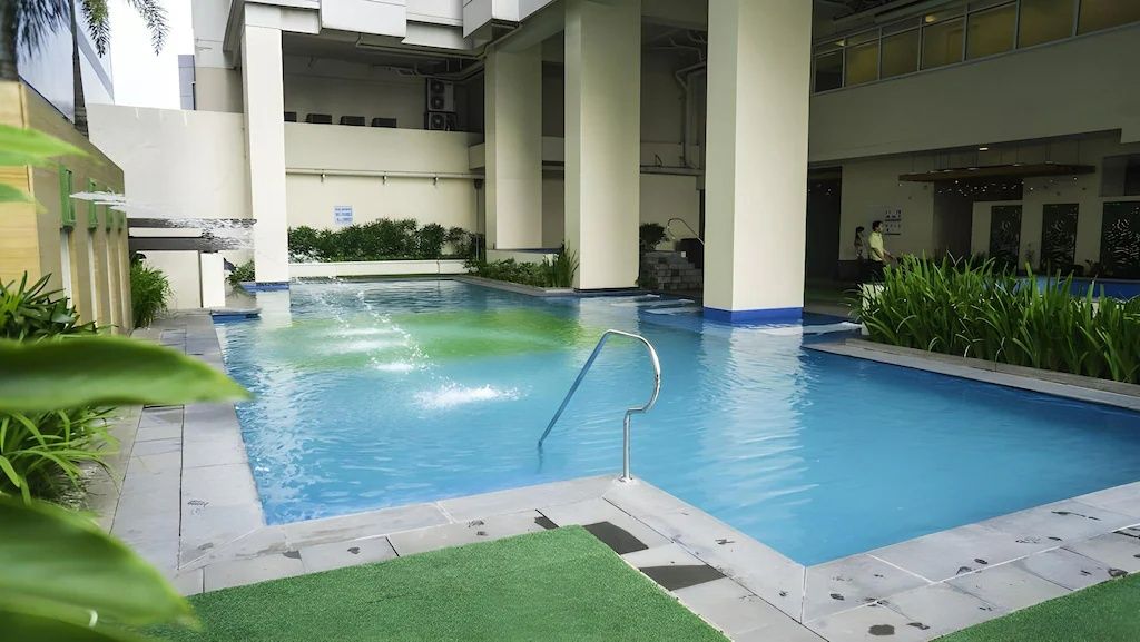 Indoor swimming pool with turquoise water, surrounded by plants and a building's pillars.