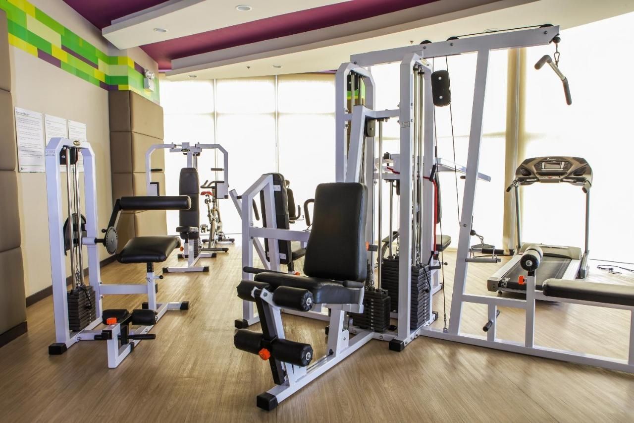 Gym with strength-training machines, mirrors, and wooden flooring in a bright room.
