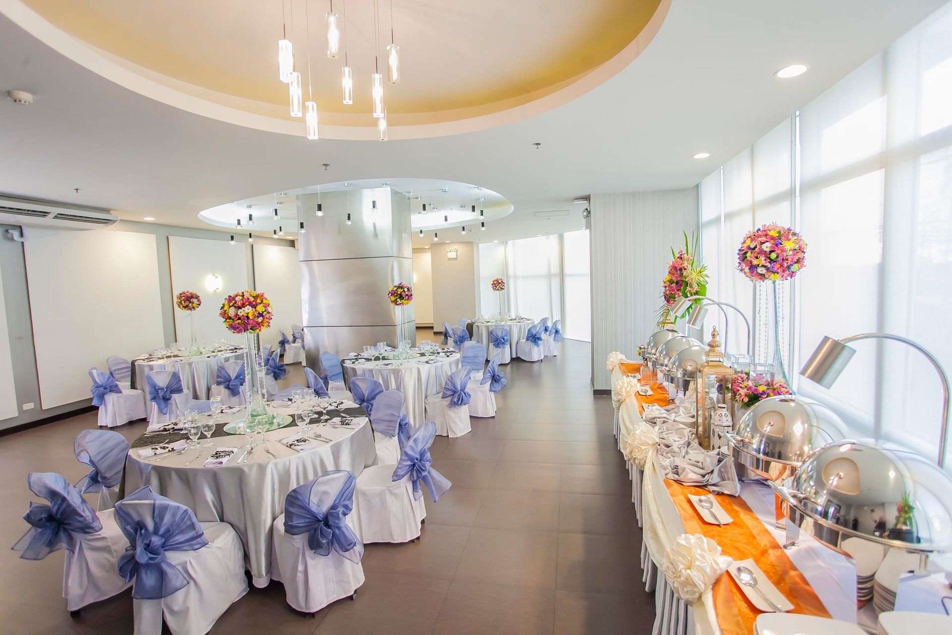 Bright banquet hall with round tables, blue chair sashes, and orange buffet setup