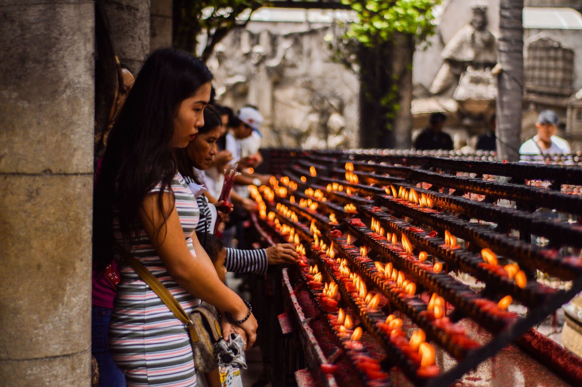 People praying beside rows of lit candles in a temple courtyard