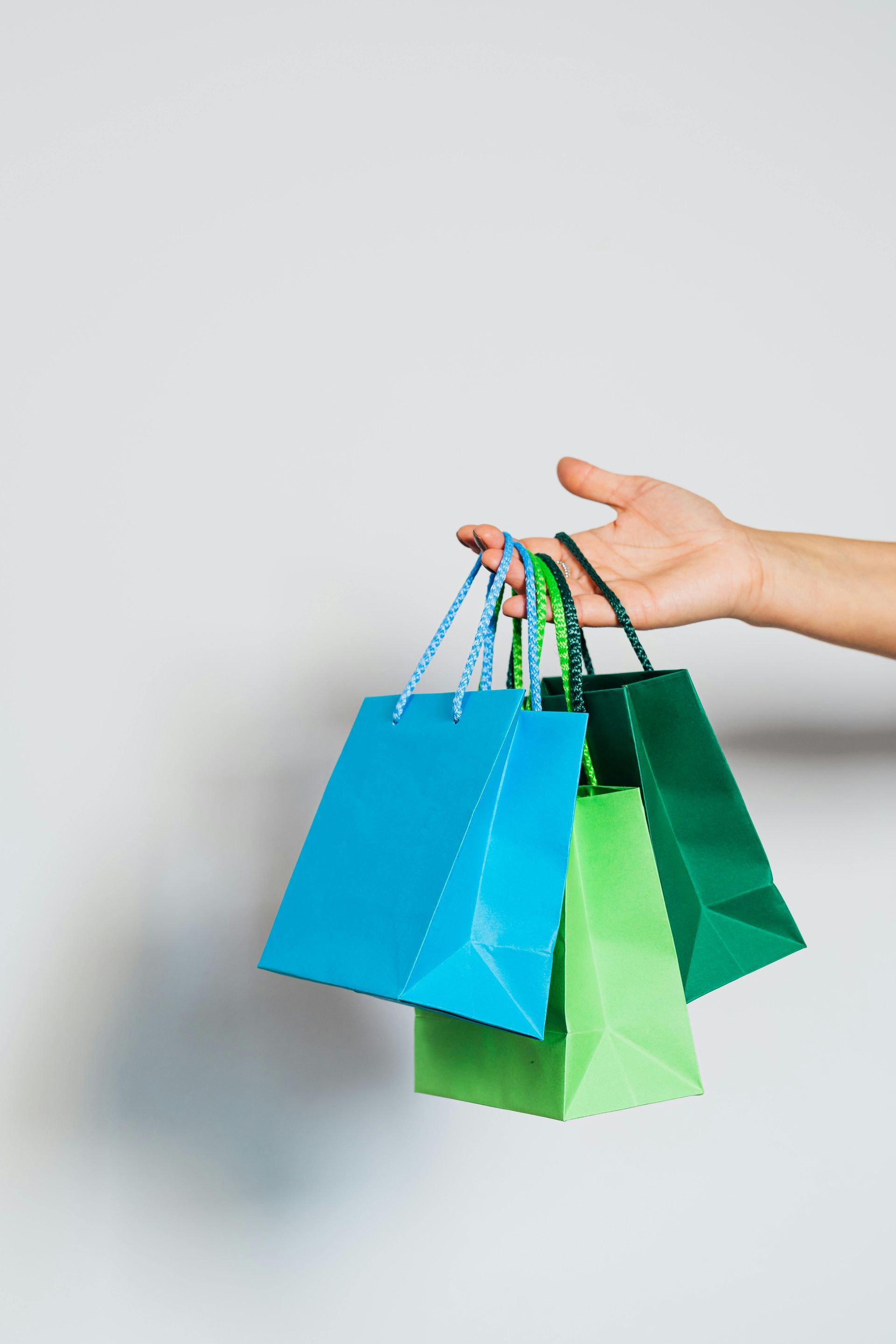 Hand holding three colorful shopping bags.