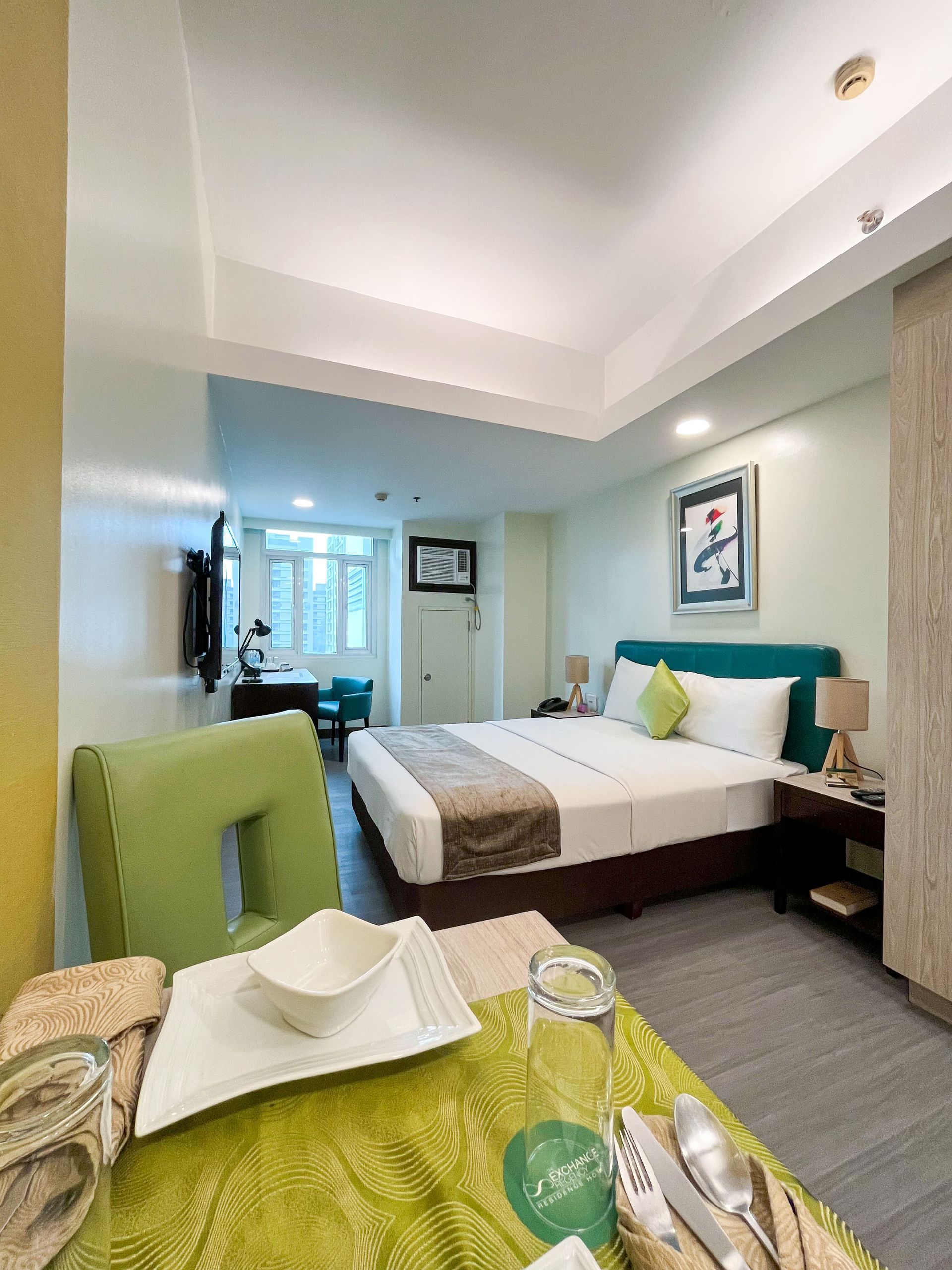Bright hotel room with queen bed and dining table at The Exchange Regency M