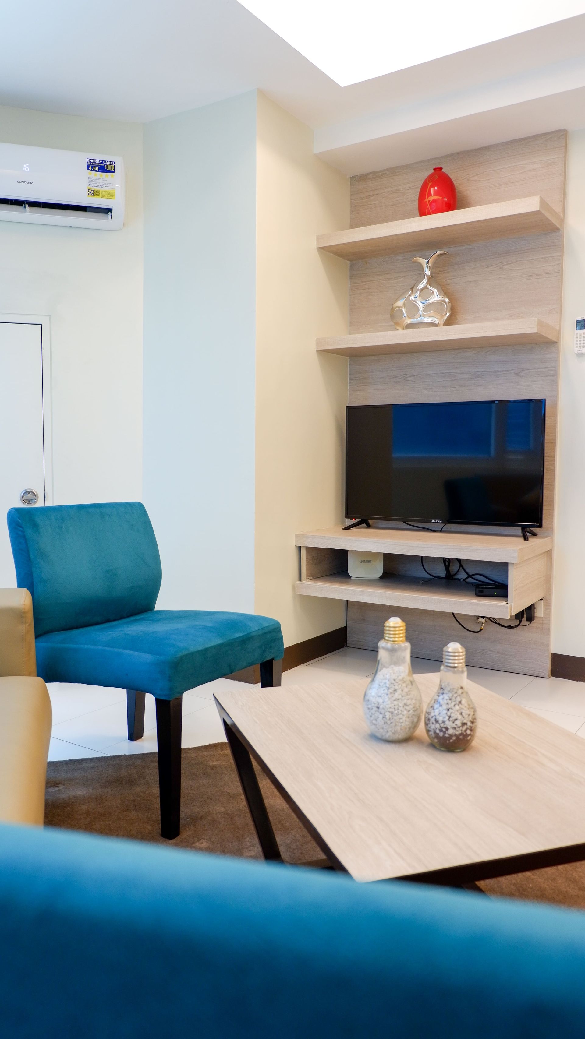 Living room with blue chair, TV on wall shelves, and coffee table.