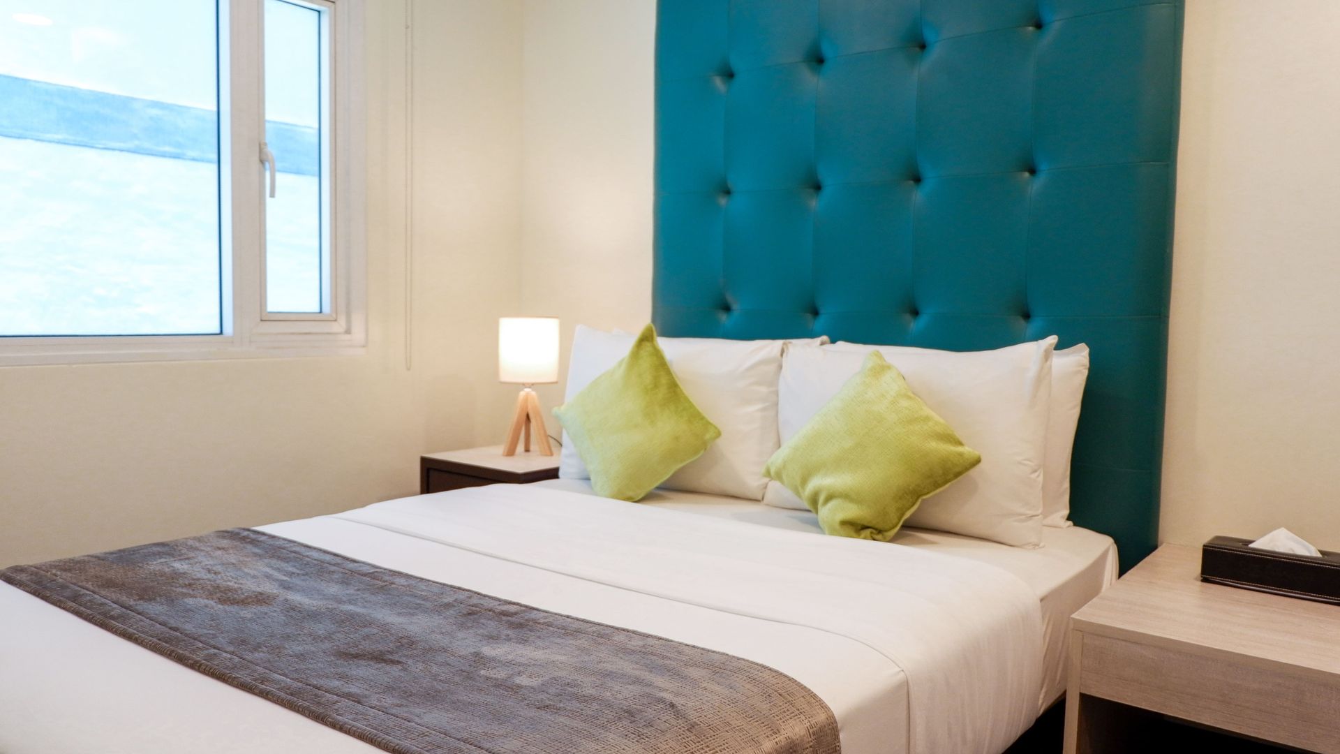 Bedroom with a teal tufted headboard, white bedding, two lime green pillows, and bedside tables.