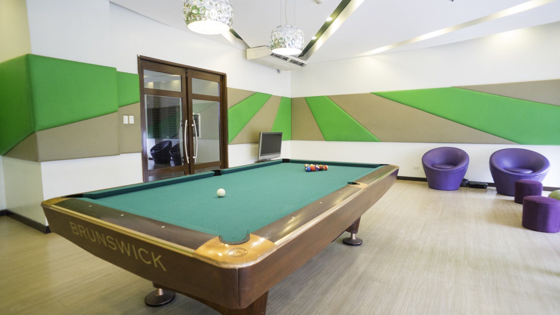 Pool table in a room with green and tan accents, purple chairs, and glass doors.