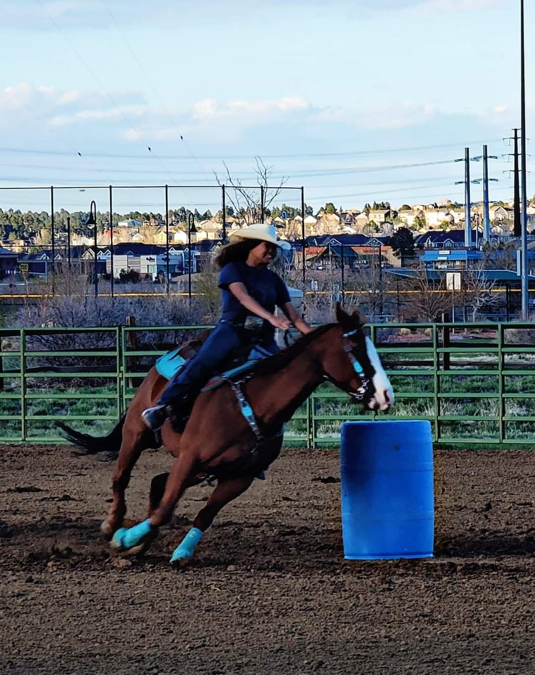Woman on a brown horse rounding a blue barrel in a rodeo arena.