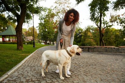 Woman with curly hair standing with a yellow Labrador on a cobblestone path in a park