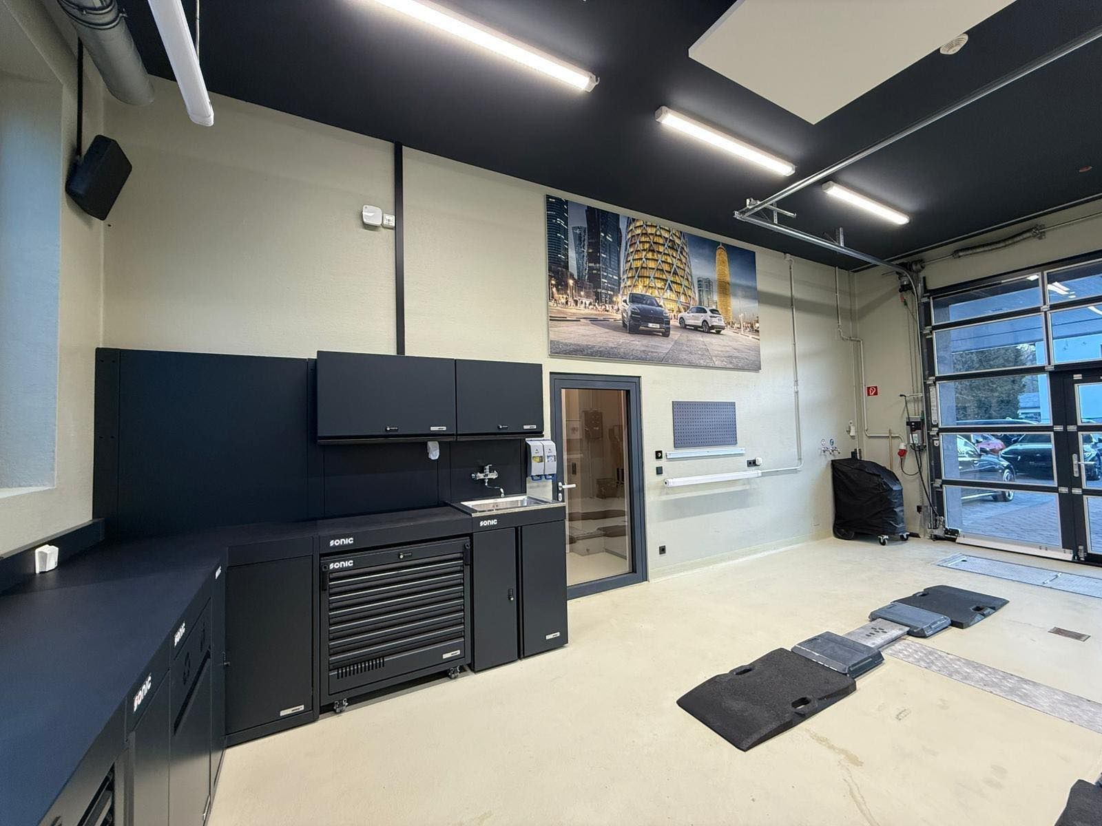 Moderne Garage mit schwarzen Schränken, Wandbildern und nach außen offenen Glastüren.