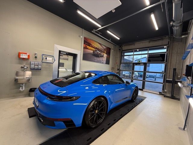 Ein blauer Sportwagen steht in einer modernen Garage mit großen Glastüren und an der Wand montierten Geräten.