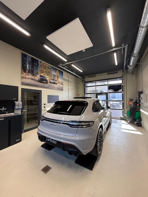 Silberner SUV in einer modernen Autowerkstatt mit schwarzer Deckenbeleuchtung und einem gläsernen Rolltor