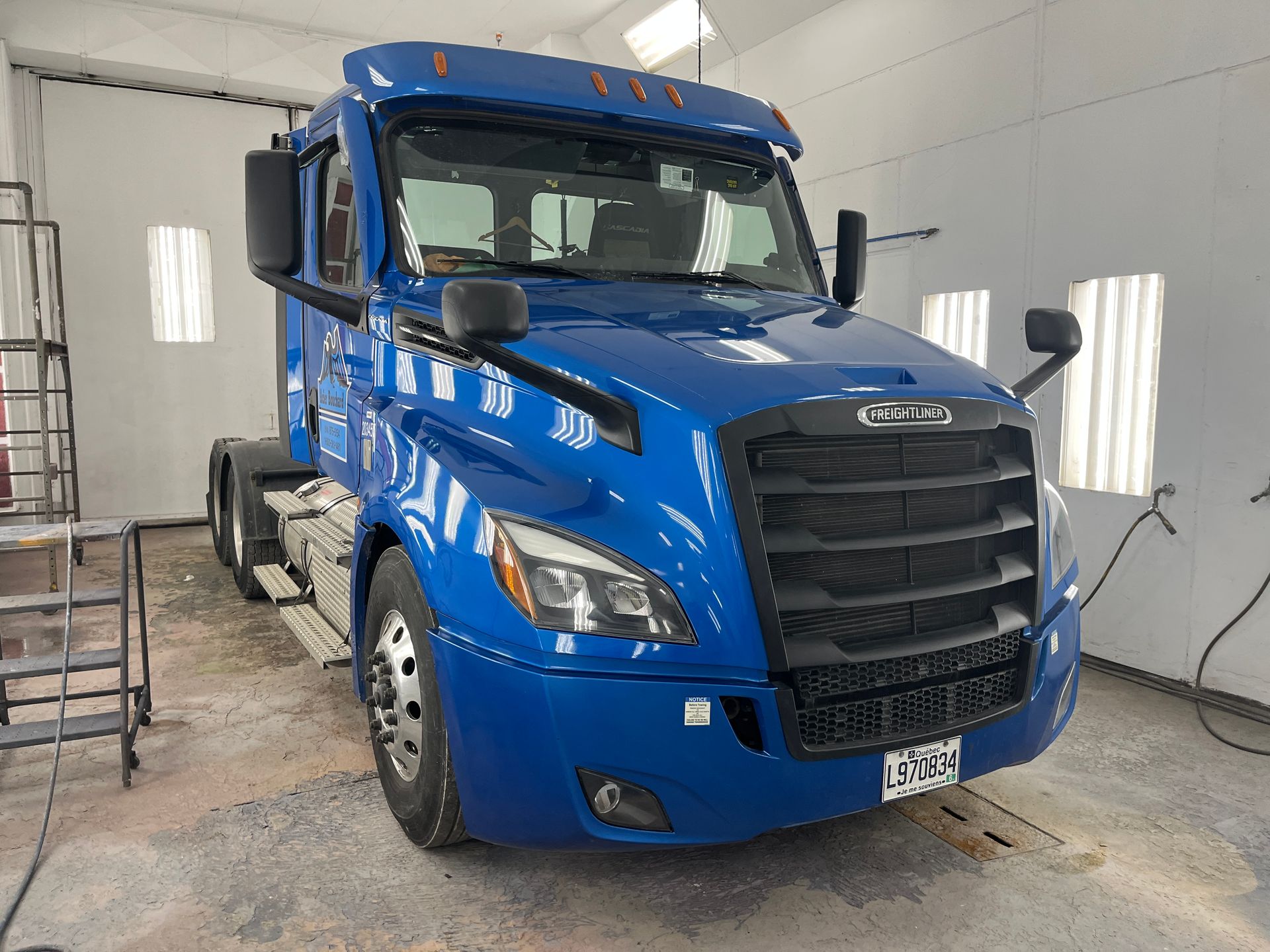 Semi-camion Freightliner bleu dans une cabine de peinture ; vue de face.