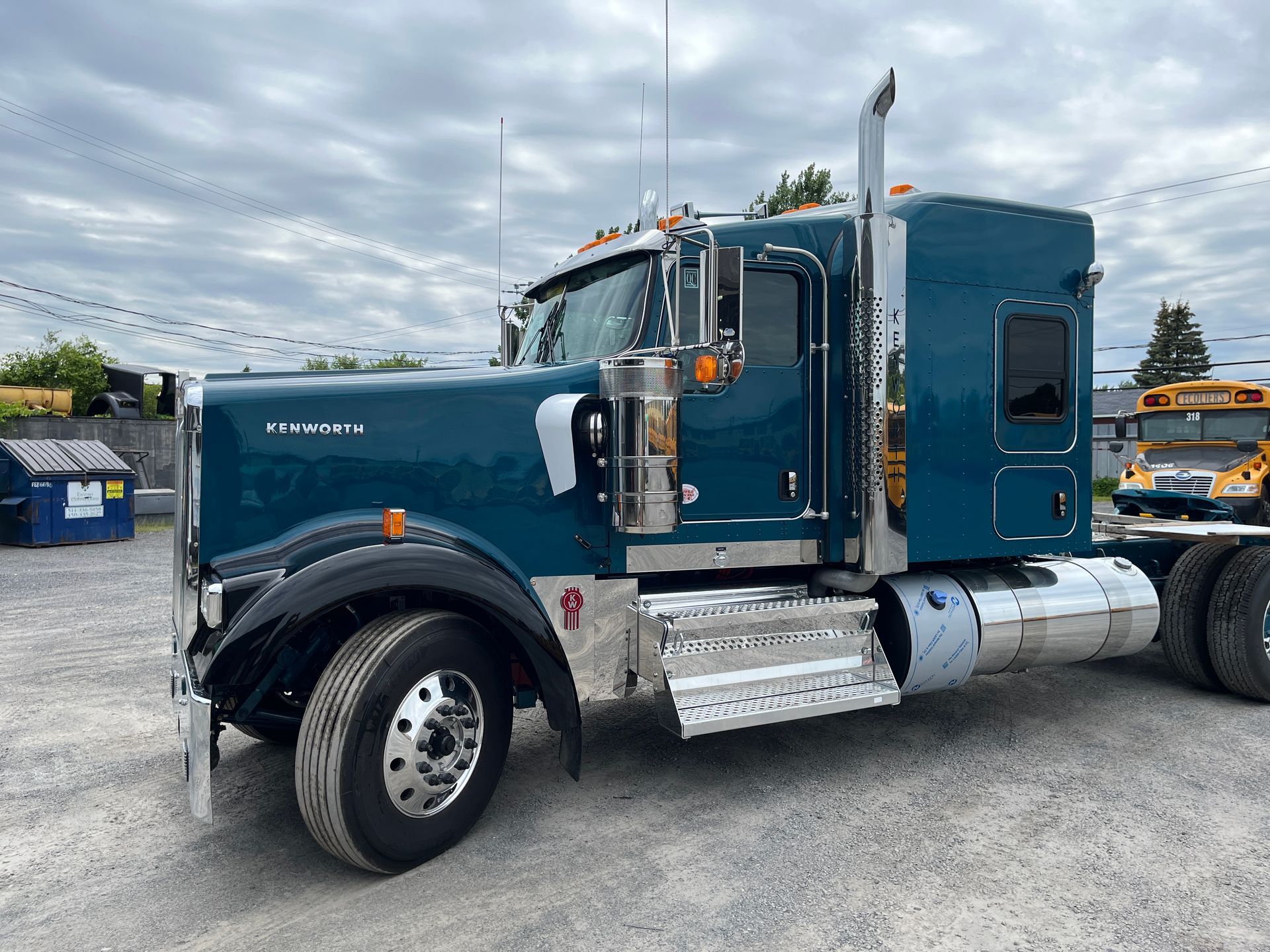 Semi-remorque bleu stationné dehors par temps couvert. Des touches de chrome et un emblème Kenworth sont visibles.