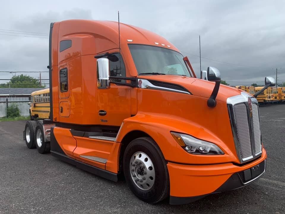 Semi-camion orange stationné sur une surface grise, devant une clôture.