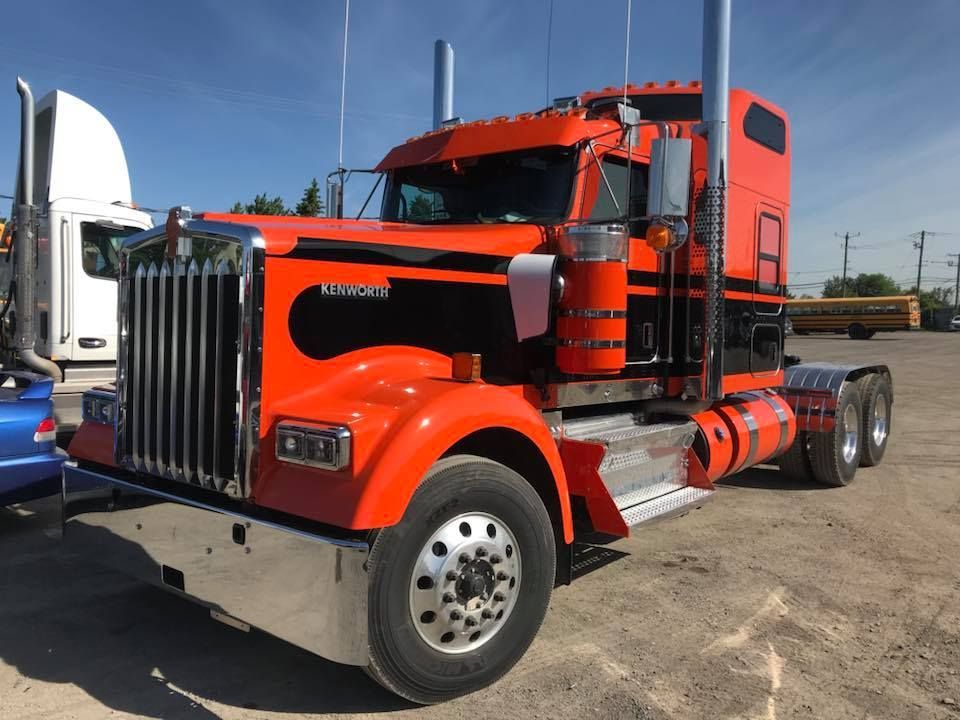 Semi-camion Kenworth orange avec des accents noirs garé à l'extérieur par une journée ensoleillée.