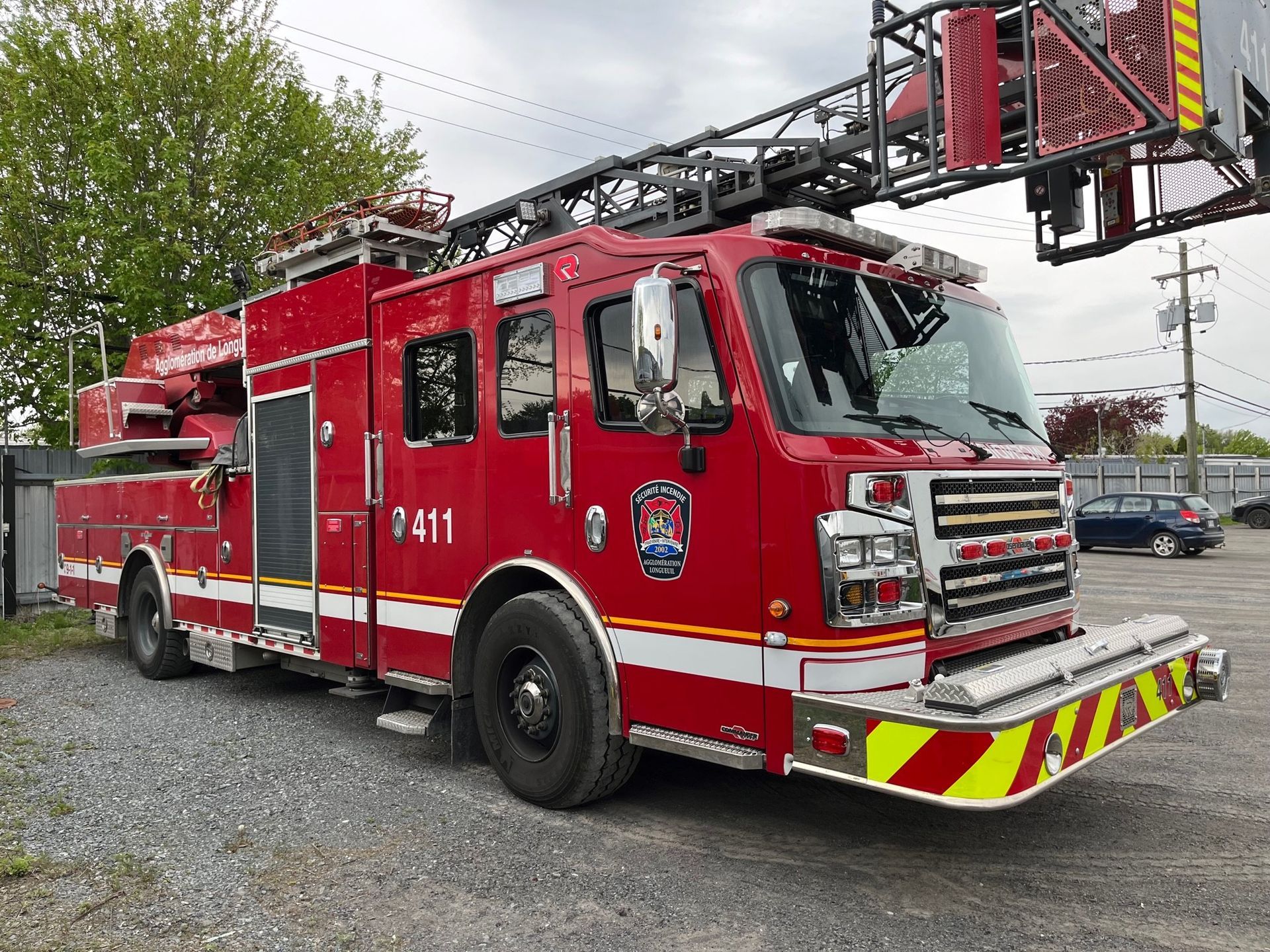 Un camion de pompiers rouge est garé dehors. Il est équipé d'une échelle et d'un pare-chocs jaune et blanc.