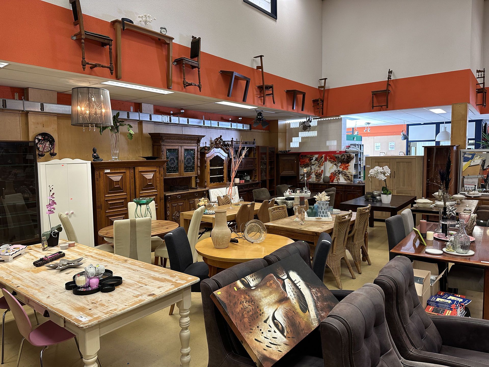 Een showroom vol meubels, tafels, stoelen, lampen en decoratie onder een oranje tussenverdieping.
