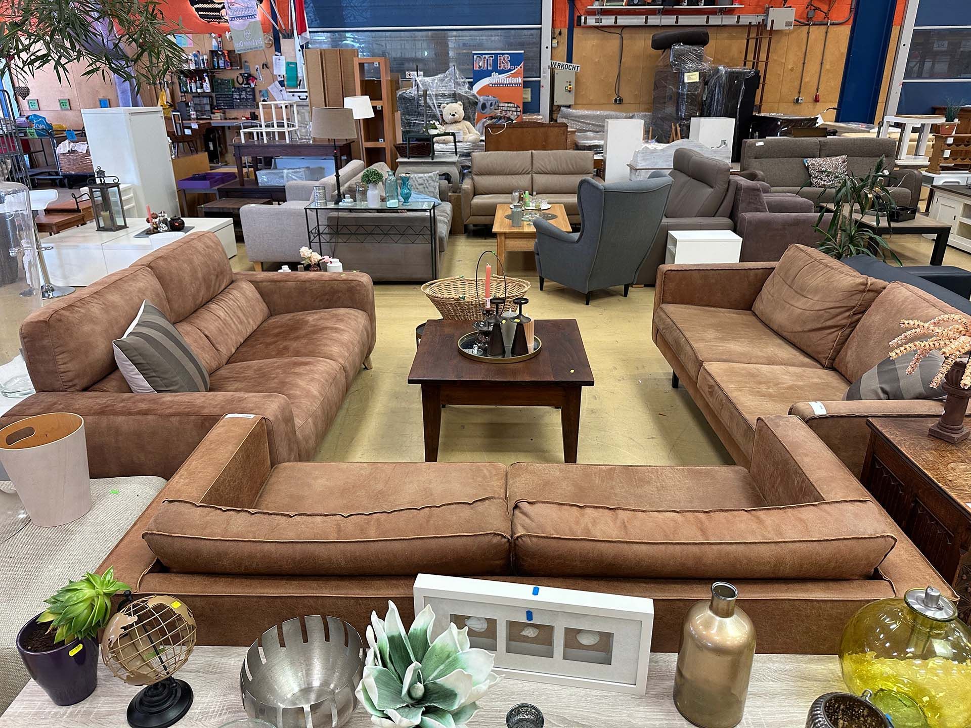 Woonkamermeubels met beige banken, fauteuils en een salontafel in een showroom.