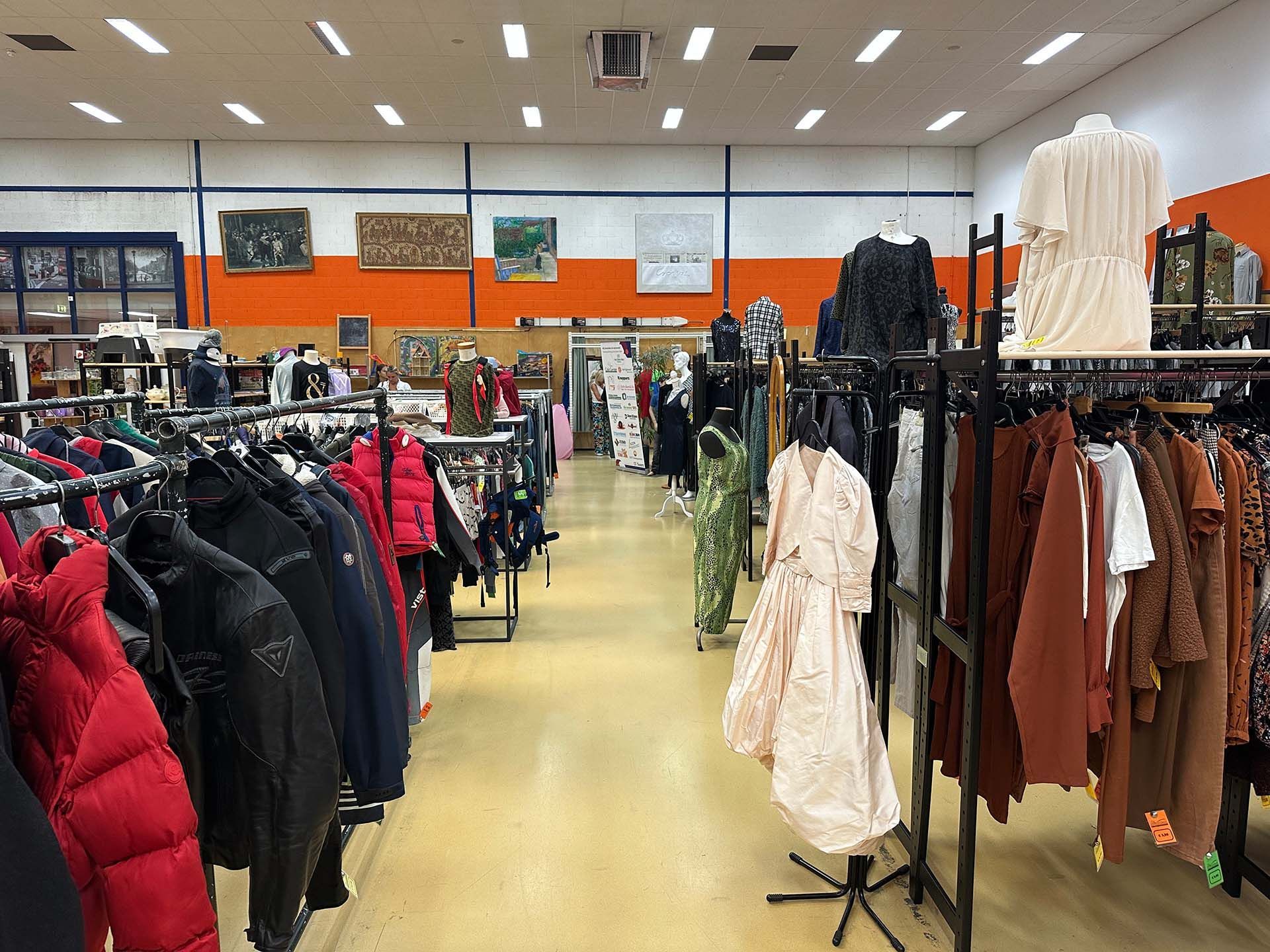 Kledingwinkelgang met rekken vol winterjassen en jurken onder fel verlicht plafond.