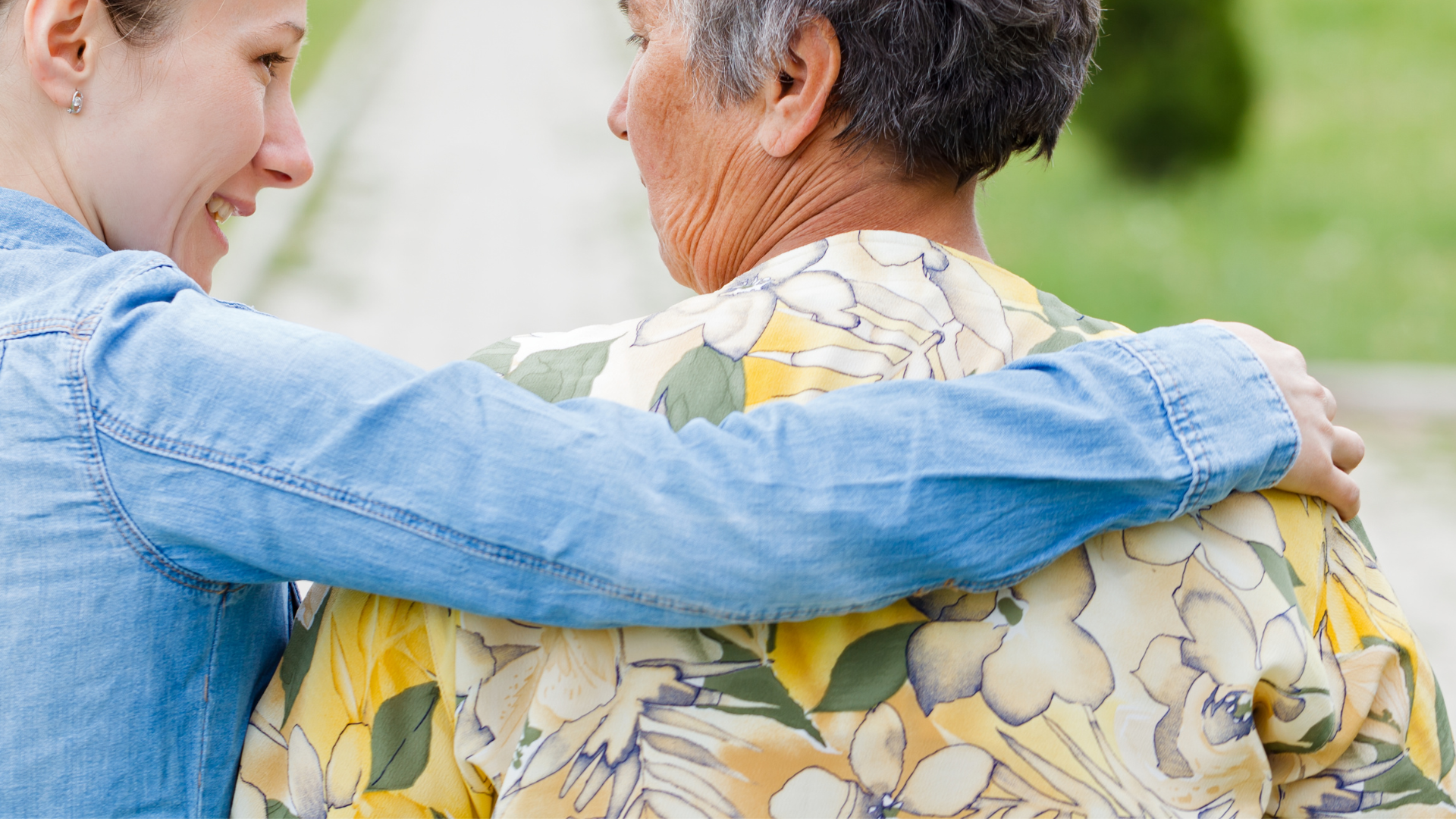 Young woman with arm around elderly woman, smiling, walking outdoors.