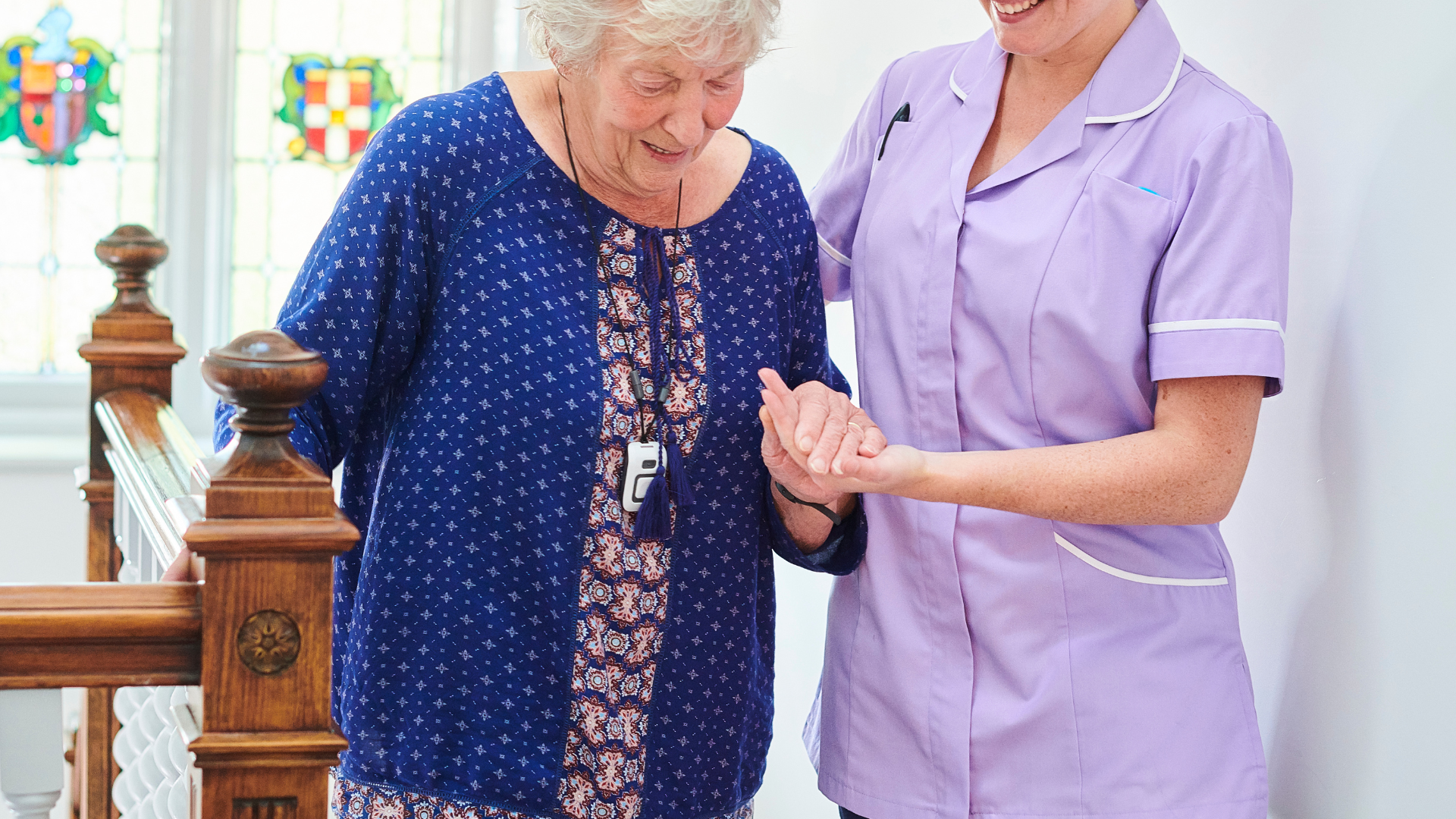 Elderly woman and caregiver on stairs, woman holding handrail and caregiver's arm.