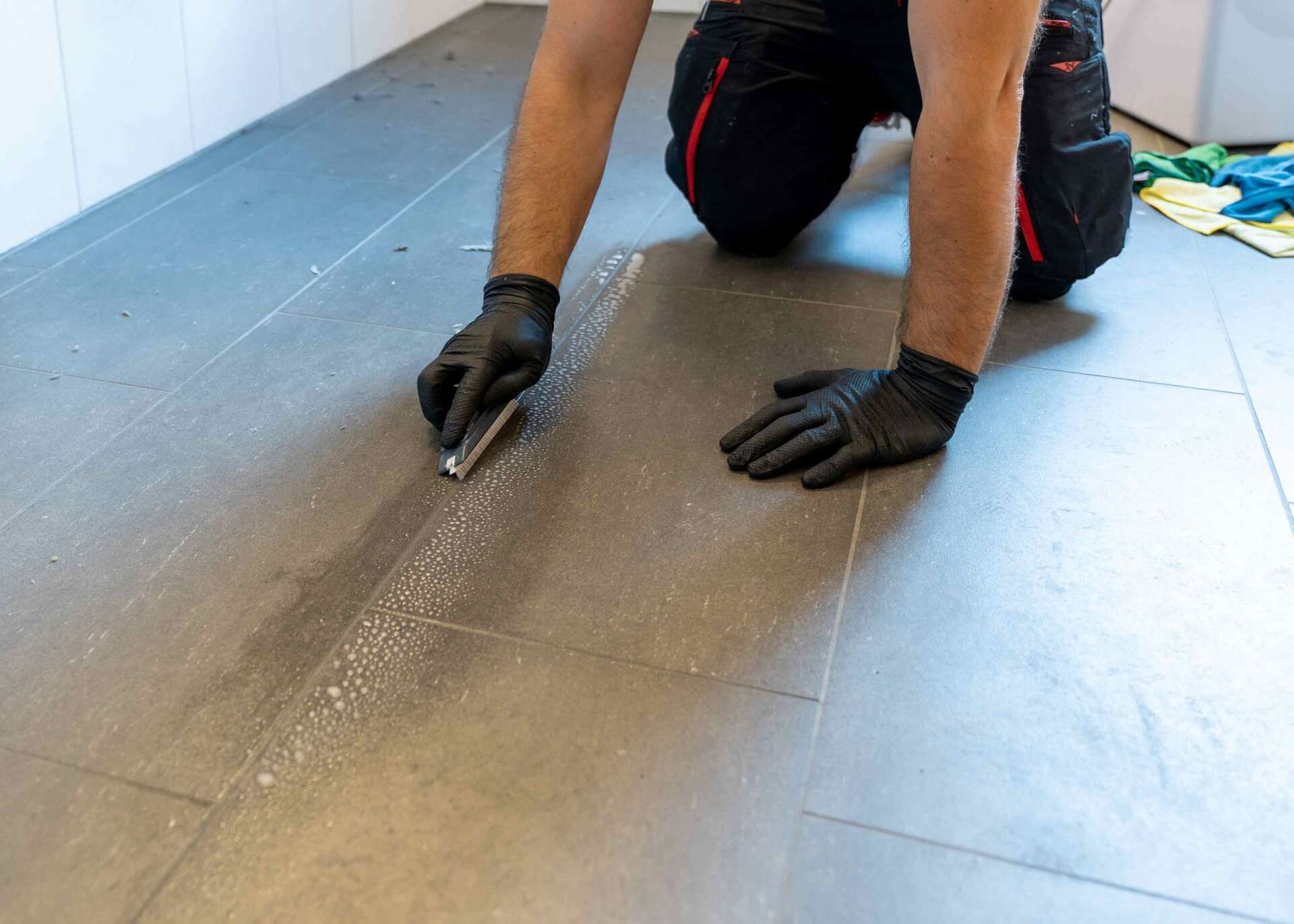 A man is kneeling on the floor cleaning a tile floor.