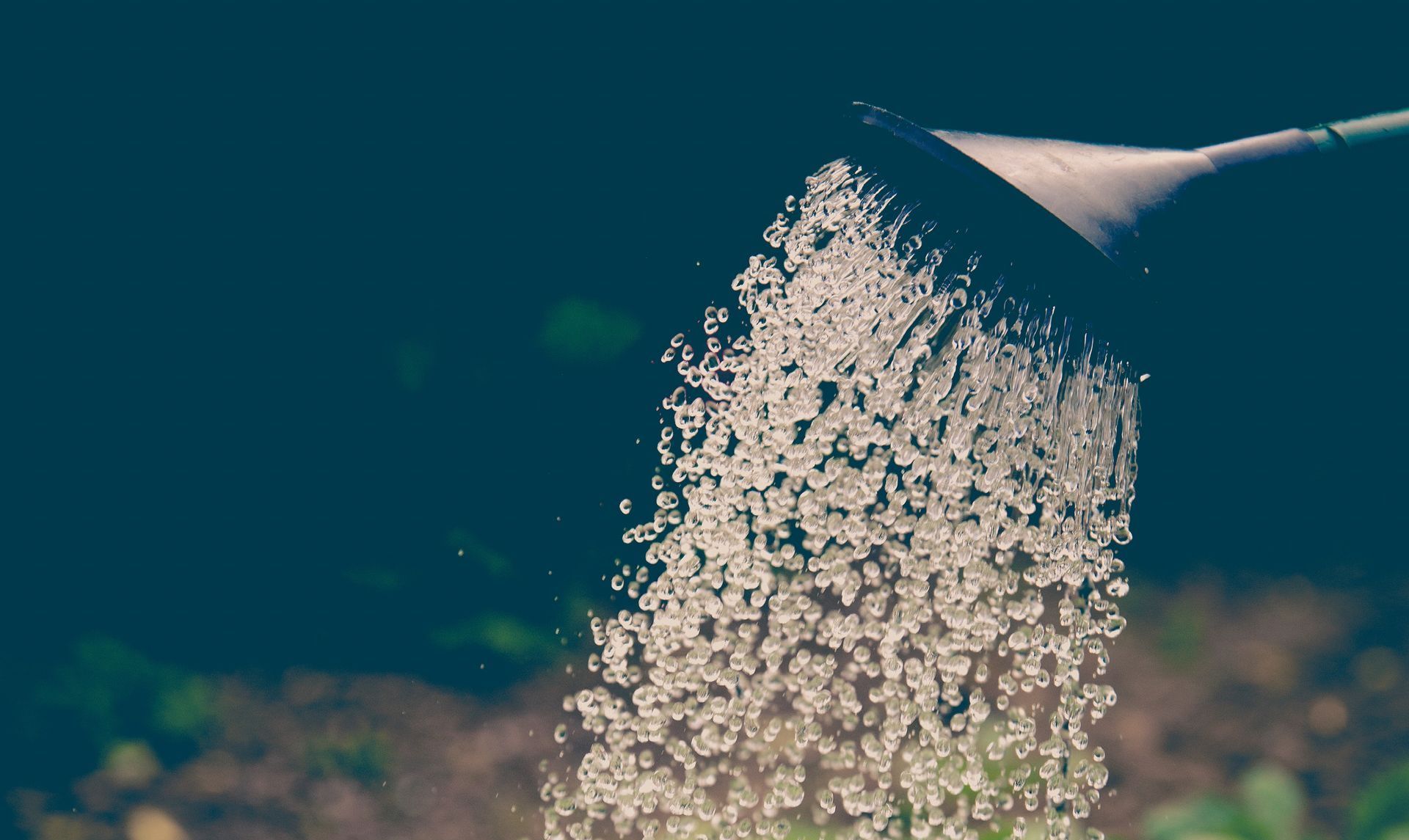 Water pouring from a watering can's spout, against a dark background.