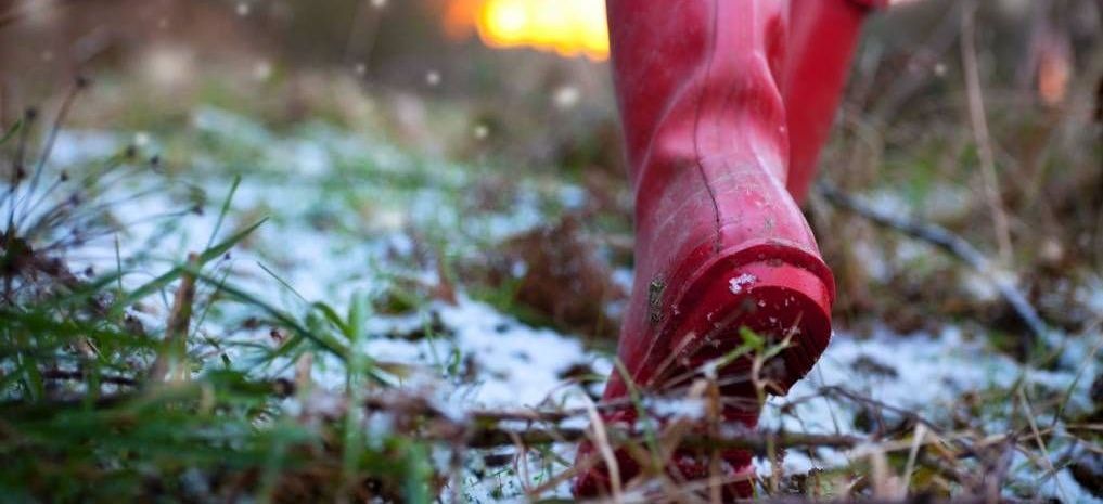 Red rain boots walking on grass and snow.