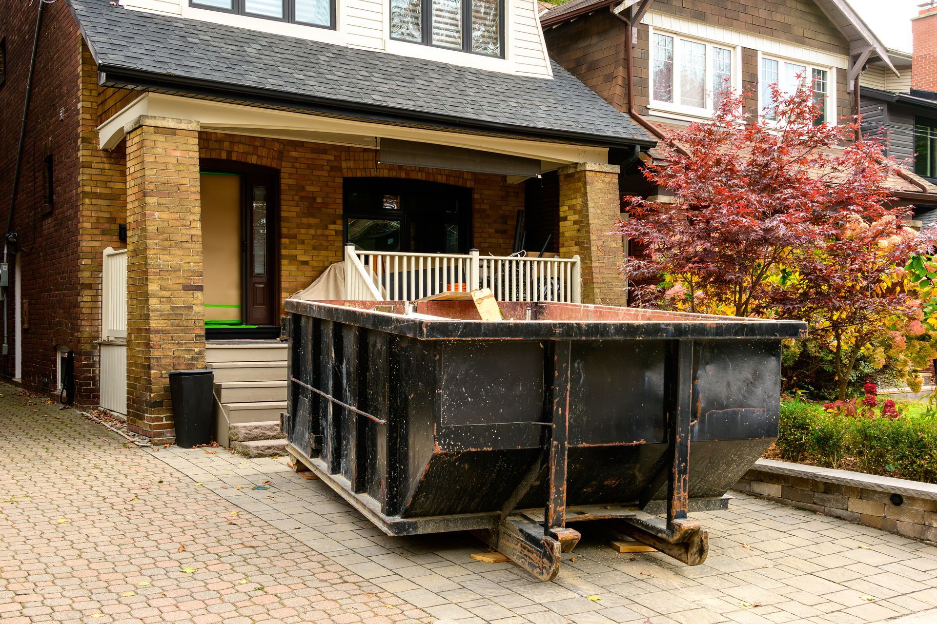 A black roll-off dumpster outside a residential renovation project in a neighborhood.
