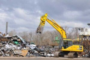 A yellow excavator is loading a pile of scrap metal into a truck.