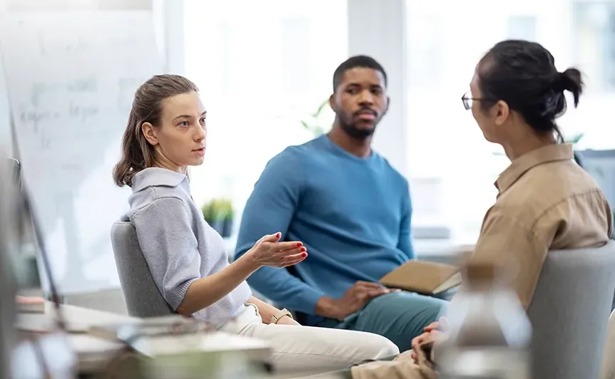 Three people in a meeting room discussing notes around a table