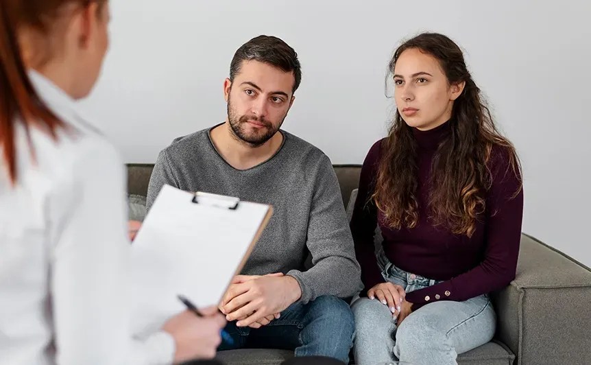Therapist speaking with a couple on a gray sofa in a bright room