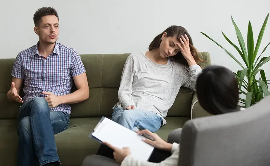 Therapist meeting with couple in a living room, one partner upset and head in hand