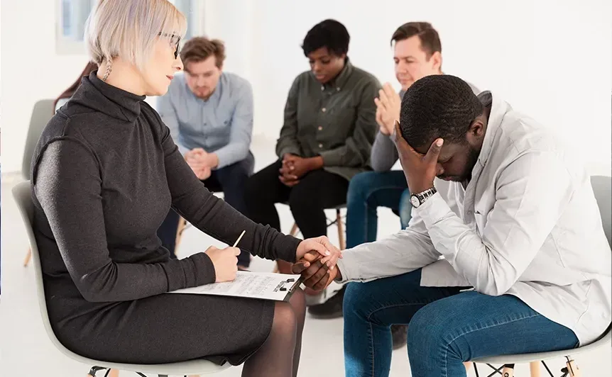 Counselor meeting with four seated clients in a bright office, one person consoling another