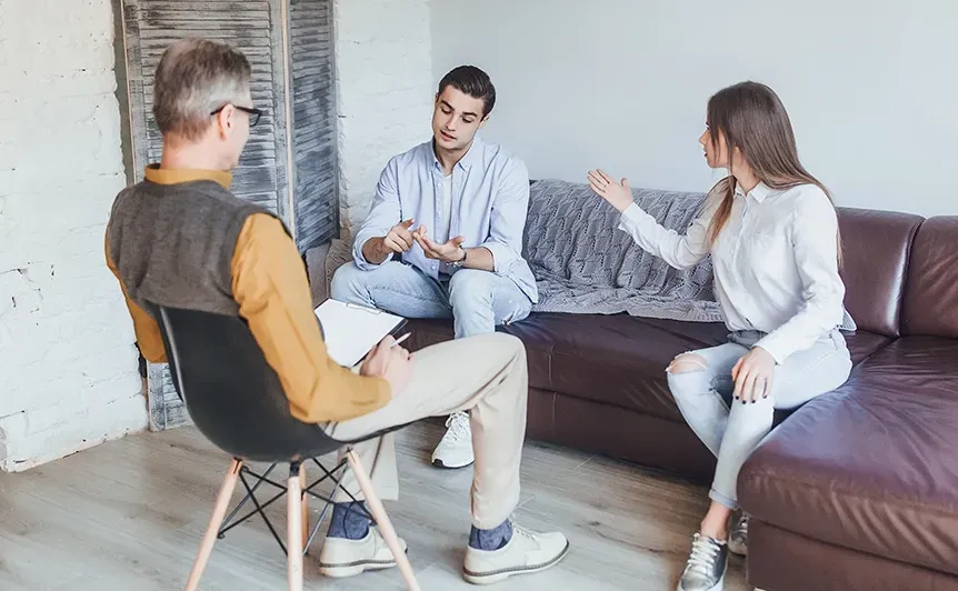 Three people in a bright office lounge talking on a couch and chair.